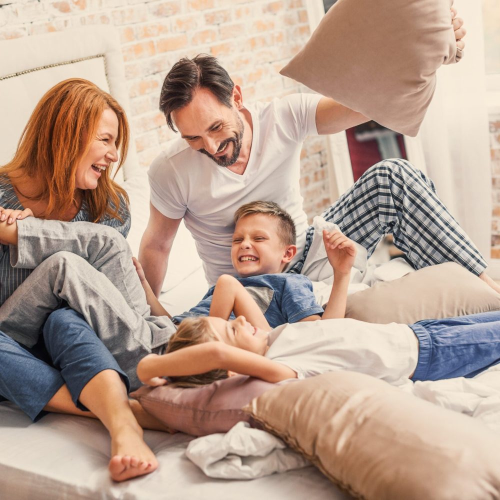 Our happy family. joyful parents spending time with their smiling children while playing with pillows in bed